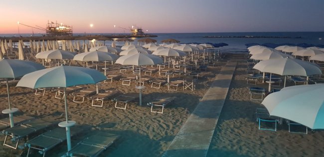 Spiaggia al tramonto con ombrelloni bianchi in fila.