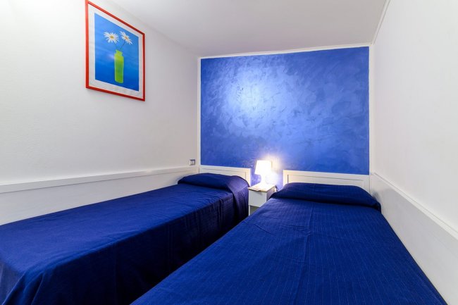 Cameretta con due letti singoli e parete blu.