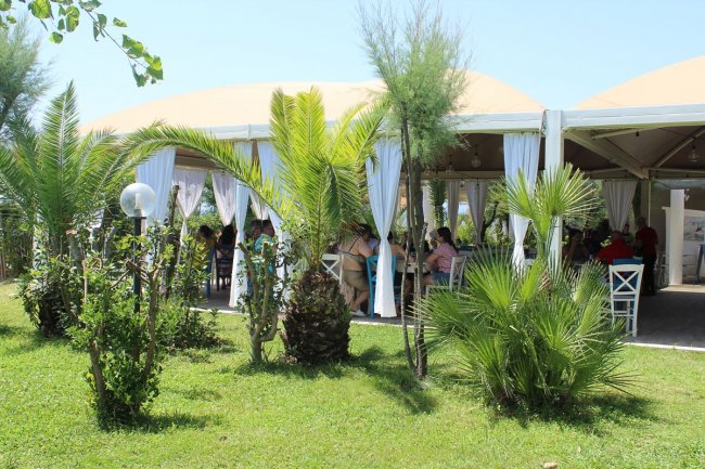 Terrazza coperta con tende bianche e ospiti seduti.