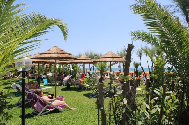 Lettini su prato con ombrelloni di paglia vicino al mare.