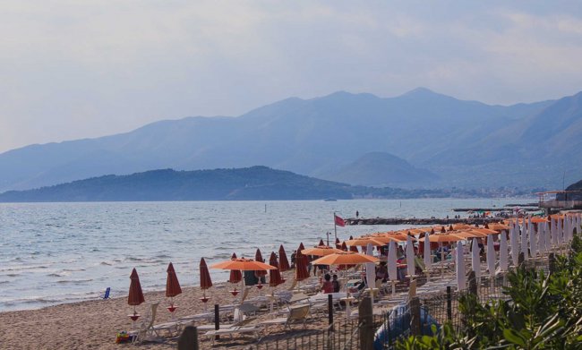 Spiaggia con ombrelloni arancioni e montagne in lontananza.