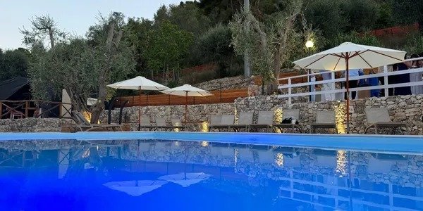 Piscina illuminata con ombrelloni e lettini.