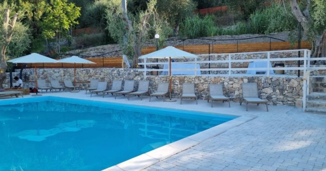 Piscina con sedie a sdraio e ombrelloni, cinta da un muro di pietra.