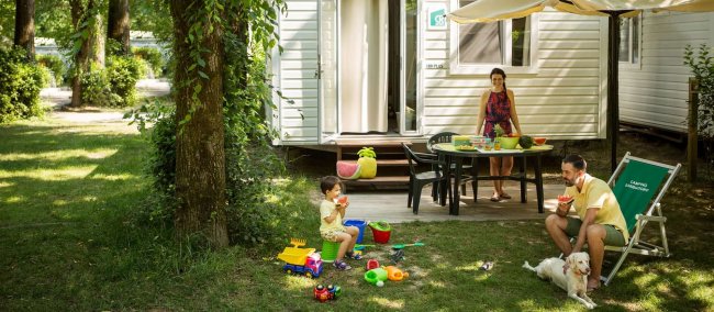 Famiglia in campeggio vicino a una roulotte, bambino gioca sul prato.