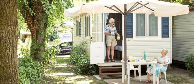 Coppia di anziani fuori da una roulotte, donna versa una bevanda.