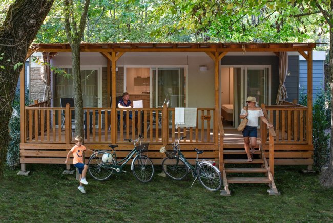 Famiglia e biciclette su un patio davanti a una roulotte in legno.