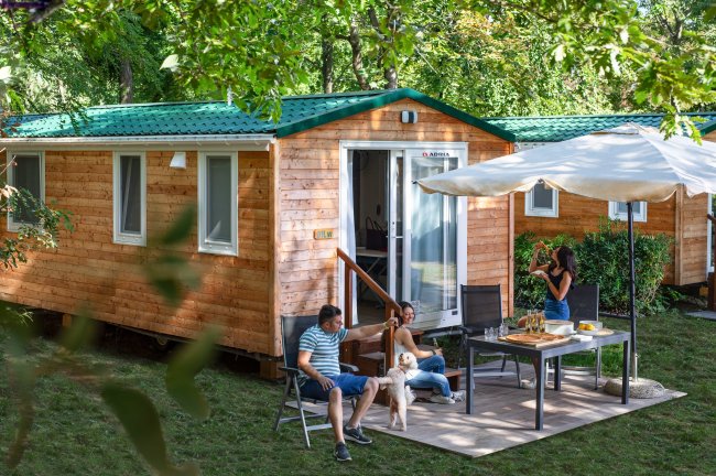 Coppia e cane all'esterno su una veranda, vicino a una roulotte in legno.