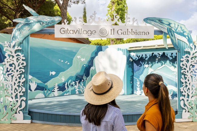 Due donne guardano palco decorato con balene.