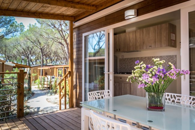 Tavolo su terrazza con fiori e vista bosco.