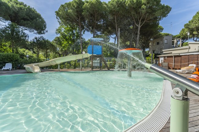 Piscina con scivolo, spruzzi d'acqua e sedie a sdraio.