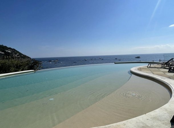 Piscina a sfioro con vista sul mare e cielo blu.