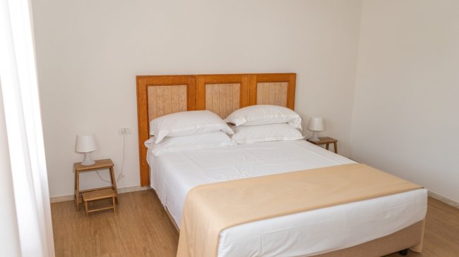 Camera con letto matrimoniale e comodini, arredata in toni bianchi e beige.