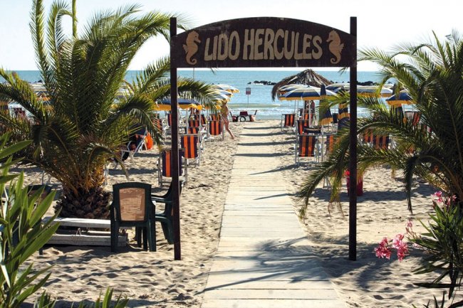 Ingresso a una spiaggia con ombrelloni e palme.