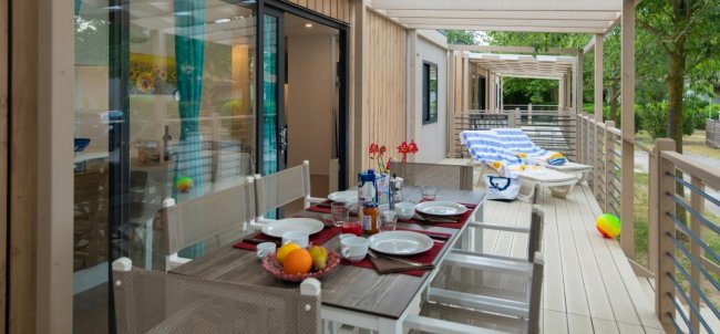 Tavolo apparecchiato su una terrazza con lettini in fondo.