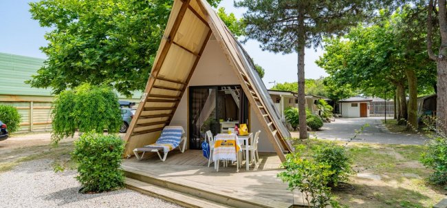 Bungalow a forma di A con terrazza tra alberi e cespugli.