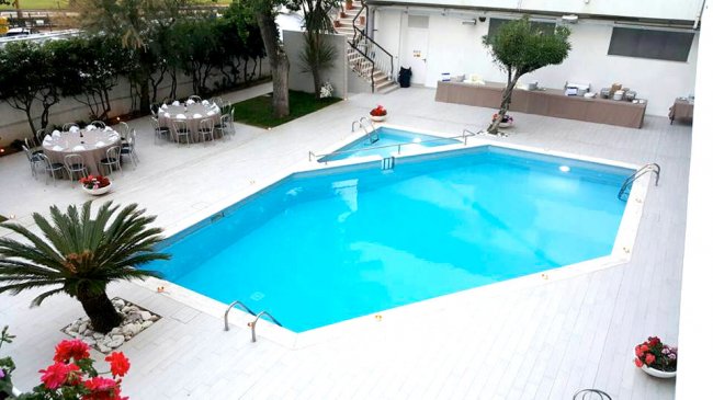 Piscina all'aperto su terrazza con tavolini apparecchiati e piante intorno.