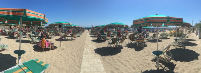 Spiaggia affollata con ombrelloni verdi e arancioni.
