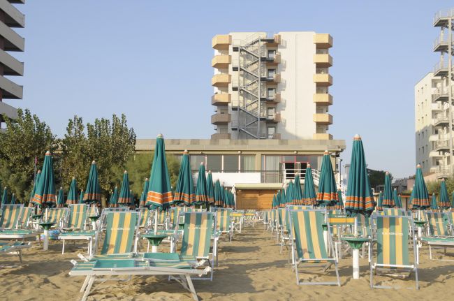 Spiaggia con lettini e ombrelloni verdi, edifici alti sullo sfondo.