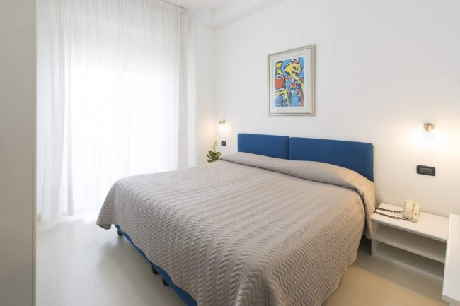 Camera da letto bianca con letto matrimoniale blu.