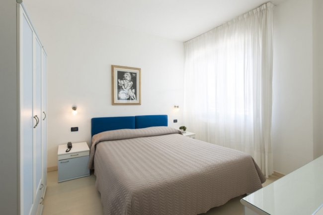 Camera da letto con letto matrimoniale, pareti bianche e testiera blu.