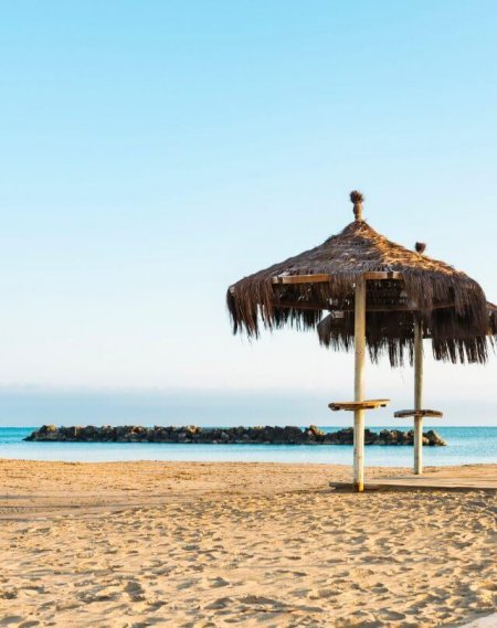 Spiaggia con sabbia dorata e due ombrelloni di paglia vicino al mare.