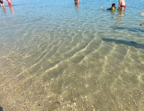 Acqua limpida al mare con alcune persone che nuotano vicino alla riva.