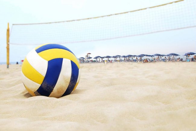Palla da volley su una spiaggia sabbiosa con rete e ombrelloni blu sullo sfondo.