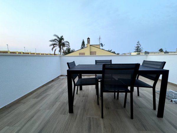 Terrazza con tavolo nero e sedie, con vista sulle palme.