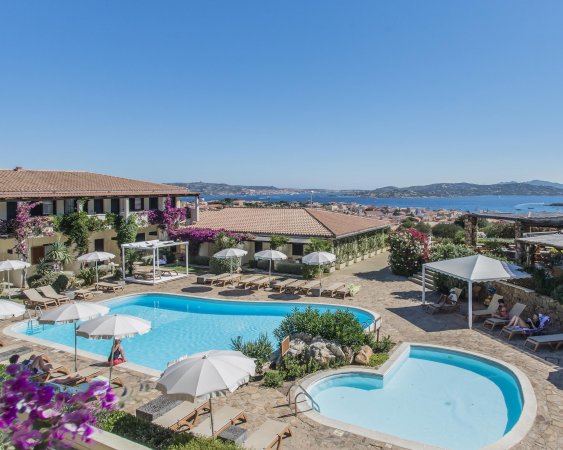 Una piscina con ombrelloni bianchi e viste panoramiche sul mare e montagne.