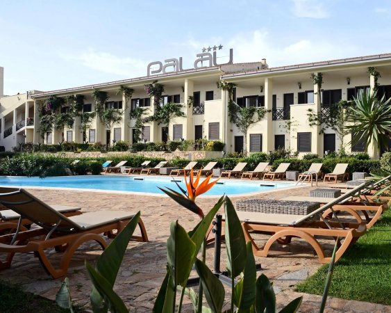 Piscina circondata da sdraio davanti a un edificio color crema con scritta 