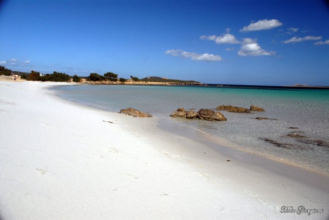 Spiaggia di sabbia bianca e mare turchese, cielo blu con nuvole sparse.