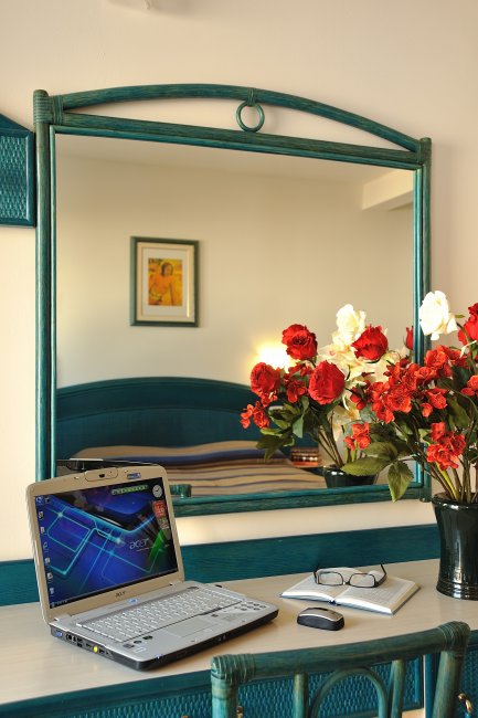 Scrivania con laptop, specchio e fiori.