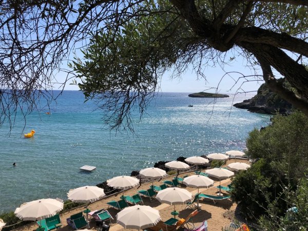 Spiaggia con ombrelloni bianchi e mare azzurro, vista di un'isola in lontananza.