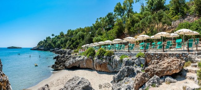Spiaggia con rocce e ombrelloni verdi.