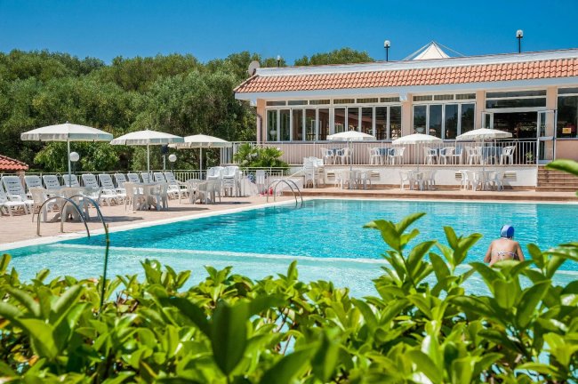 Piscina all'aperto con lettini e ombrelloni bianchi.