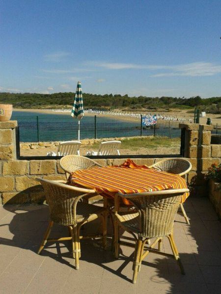 Tavolo con sedie in rattan e tovaglia arancione, vista mare.