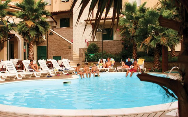 Piscina con sdraio e palme intorno.