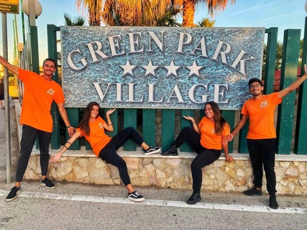 Persone in maglie arancioni posano davanti a un'insegna.