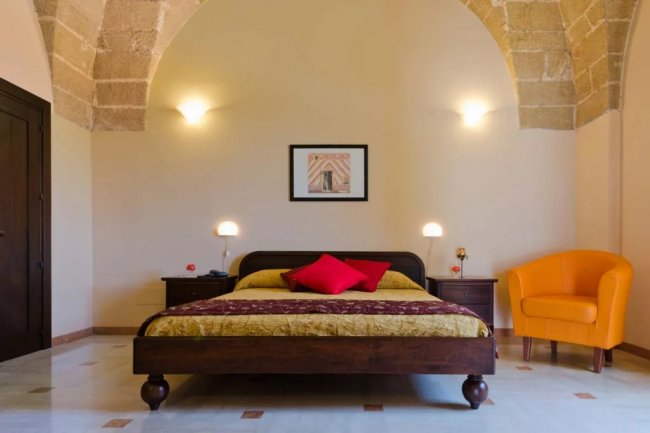 Camera con letto matrimoniale, poltrona arancione e soffitto a volta.
