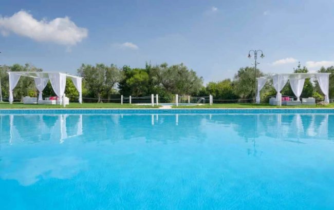 Area piscina con tende bianche e vegetazione verde sullo sfondo.