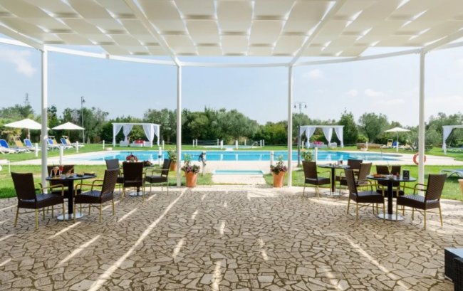 Patio con tavoli e sedie, vista sulla piscina e giardino sullo sfondo.