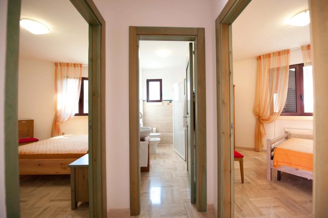 Interno di una casa con due stanze da letto e un bagno, pavimento in parquet chiaro.