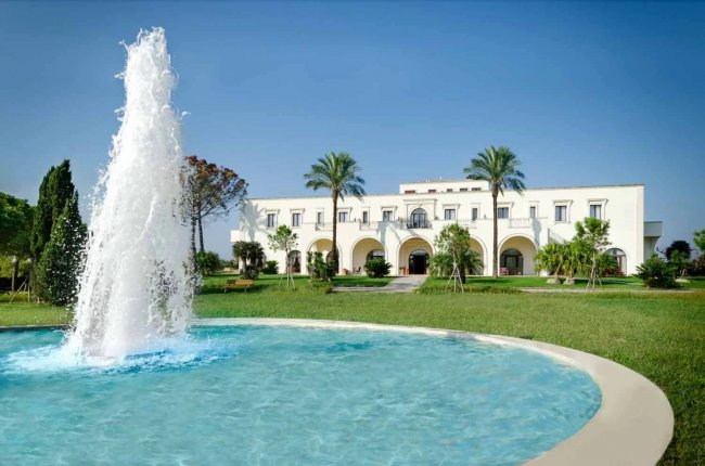 Fontana davanti a un edificio bianco con archi e palme.
