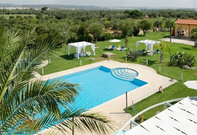 Piscina circondata da giardini, gazebo bianchi e lettini blu.