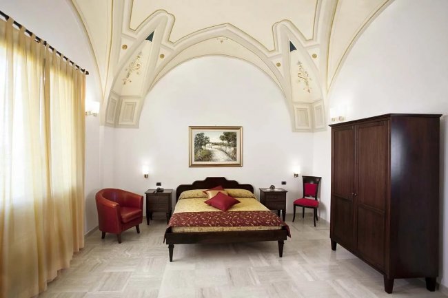 Camera da letto con soffitto a volta, letto matrimoniale, armadio scuro e sedia rossa.