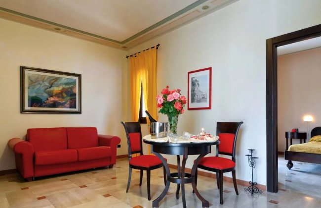 Soggiorno con divano rosso, tavolo rotondo, sedie abbinate e fiori su tavola.