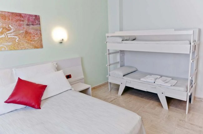 Camera con letto matrimoniale e letto a castello bianco, decorazione murale astratta.