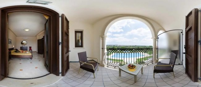 Stanza con letto e balcone arredato, vista su piscina e paesaggio.