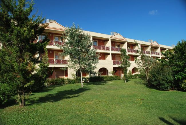 Complesso residenziale a tre piani con giardino e alberi verdi.