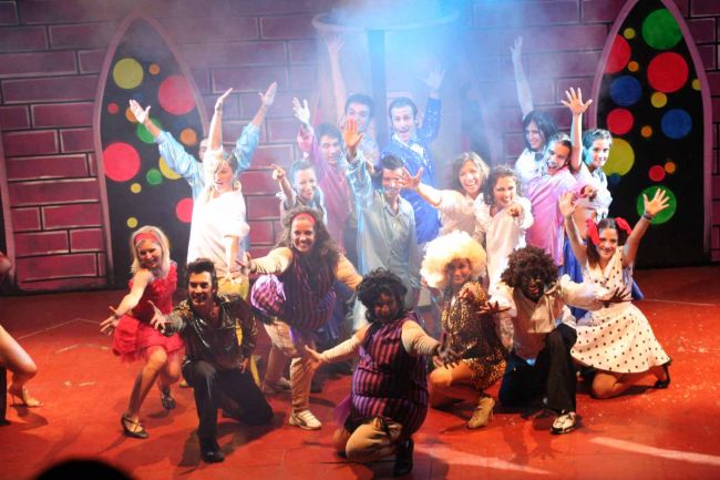 Un gruppo di persone che posa entusiasta su un palco con sfondo colorato.